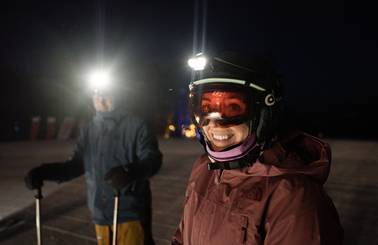 Two people in ski gear with headlamps at night