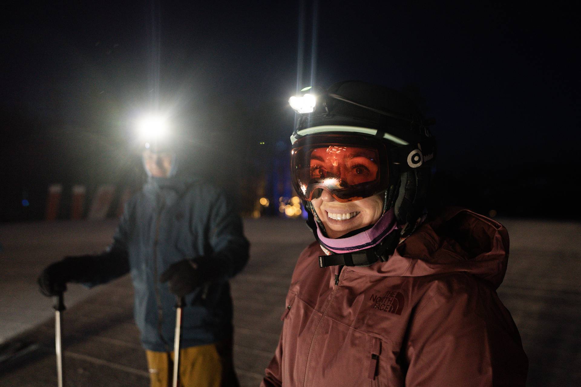 Two people in ski gear with headlamps at night