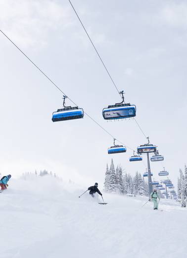 Skiers and snowboarders in powder underneath Ramcharger 8