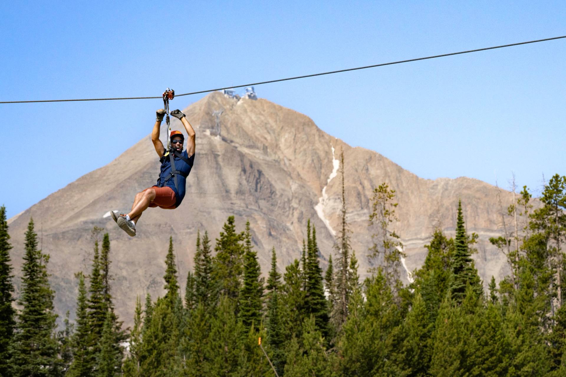 Man on a zipline in front of Lone Peak