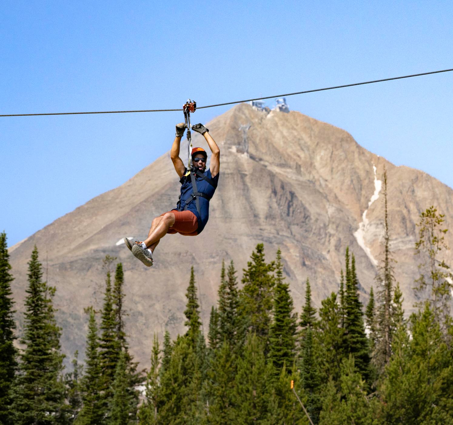 Man on a zipline in front of Lone Peak