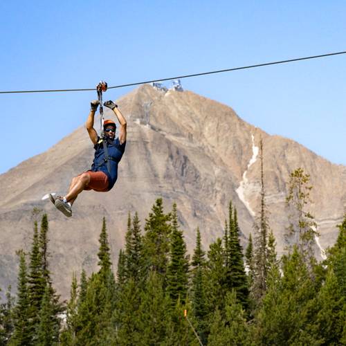 Man on a zipline with Lone Mountain in the background
