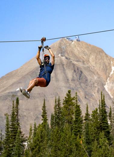 Man on a zipline in front of Lone Peak