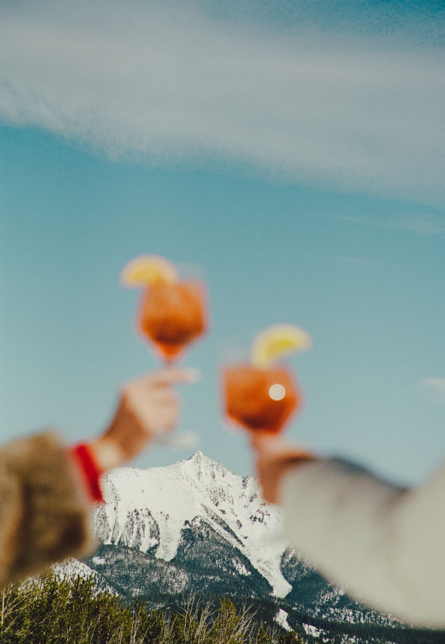 Two people cheersing cocktails in front of a mountain peak