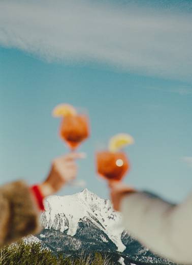 Two people cheersing cocktails in front of a mountain peak