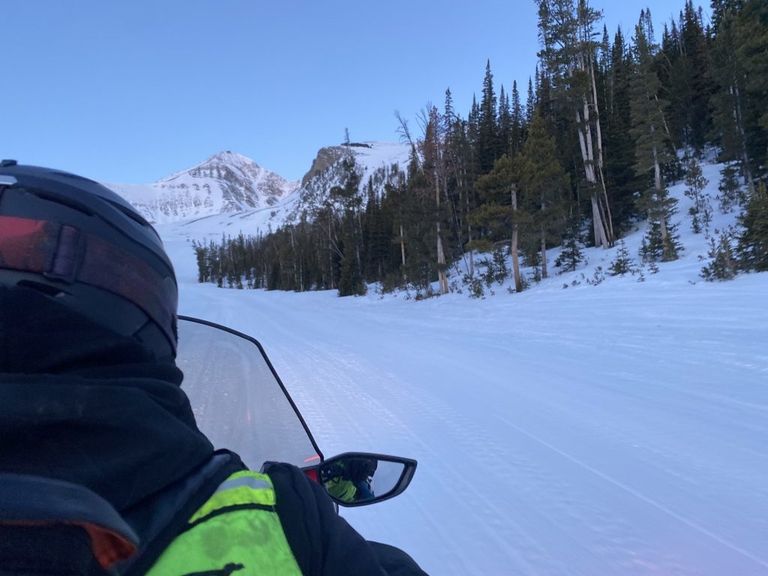 An over the shoulder shot of lift maintenance driving their snowmobile up Lone Mountain