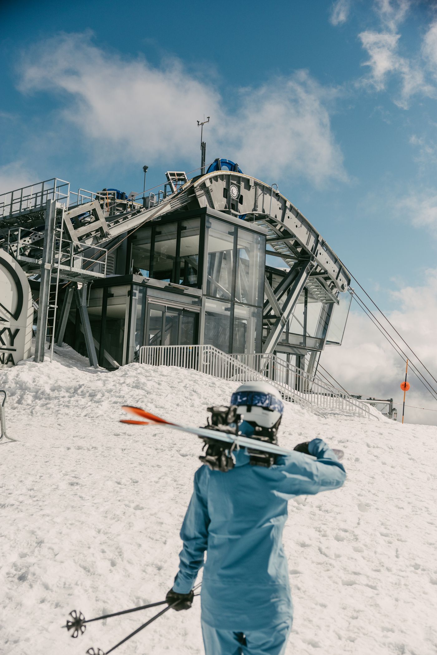 Woman in ski gear carrying her skis in front of the Lone Peak Tram