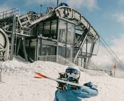 Woman in ski gear carrying her skis in front of the Lone Peak Tram