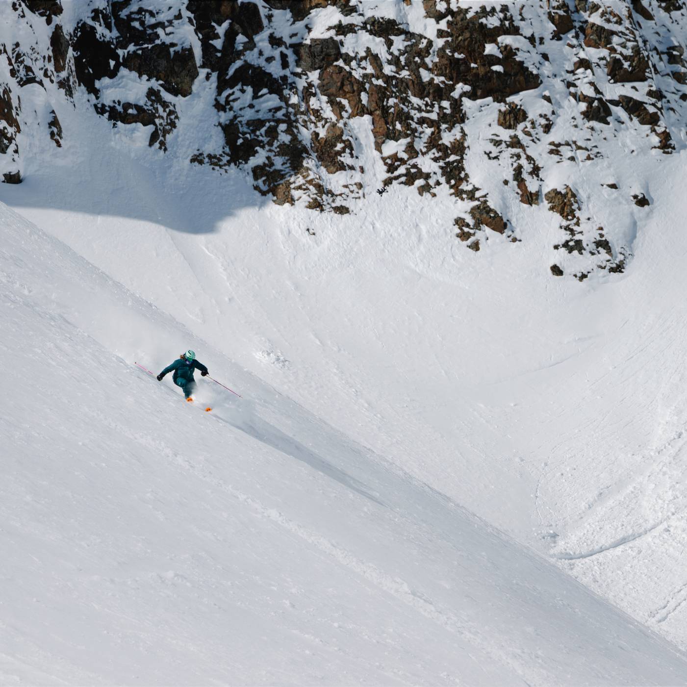 Skier in powder with cliffs in the background