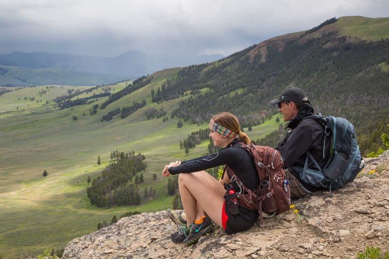 a woman and man sit on a ridge overlooking a valley