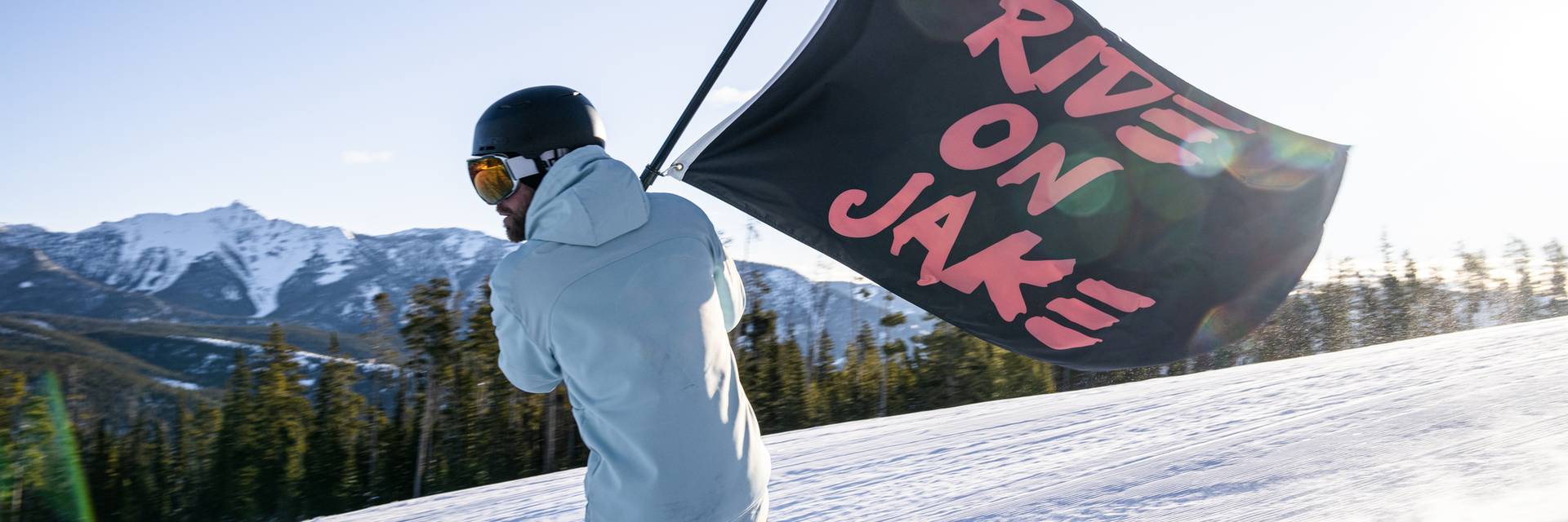 Snowboarder with a flag reading "Ride On Jake"