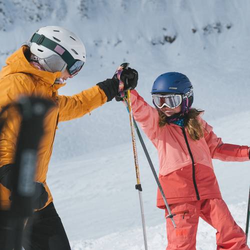 Girl and her parent in ski gear high-fiving