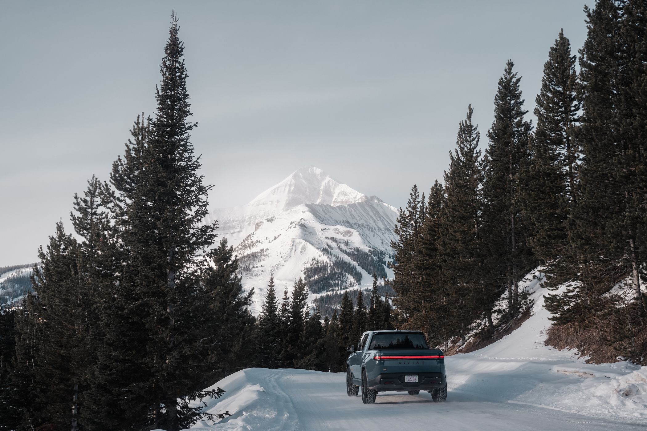 Rivian truck on a snowy road with Big Sky Resort in the background