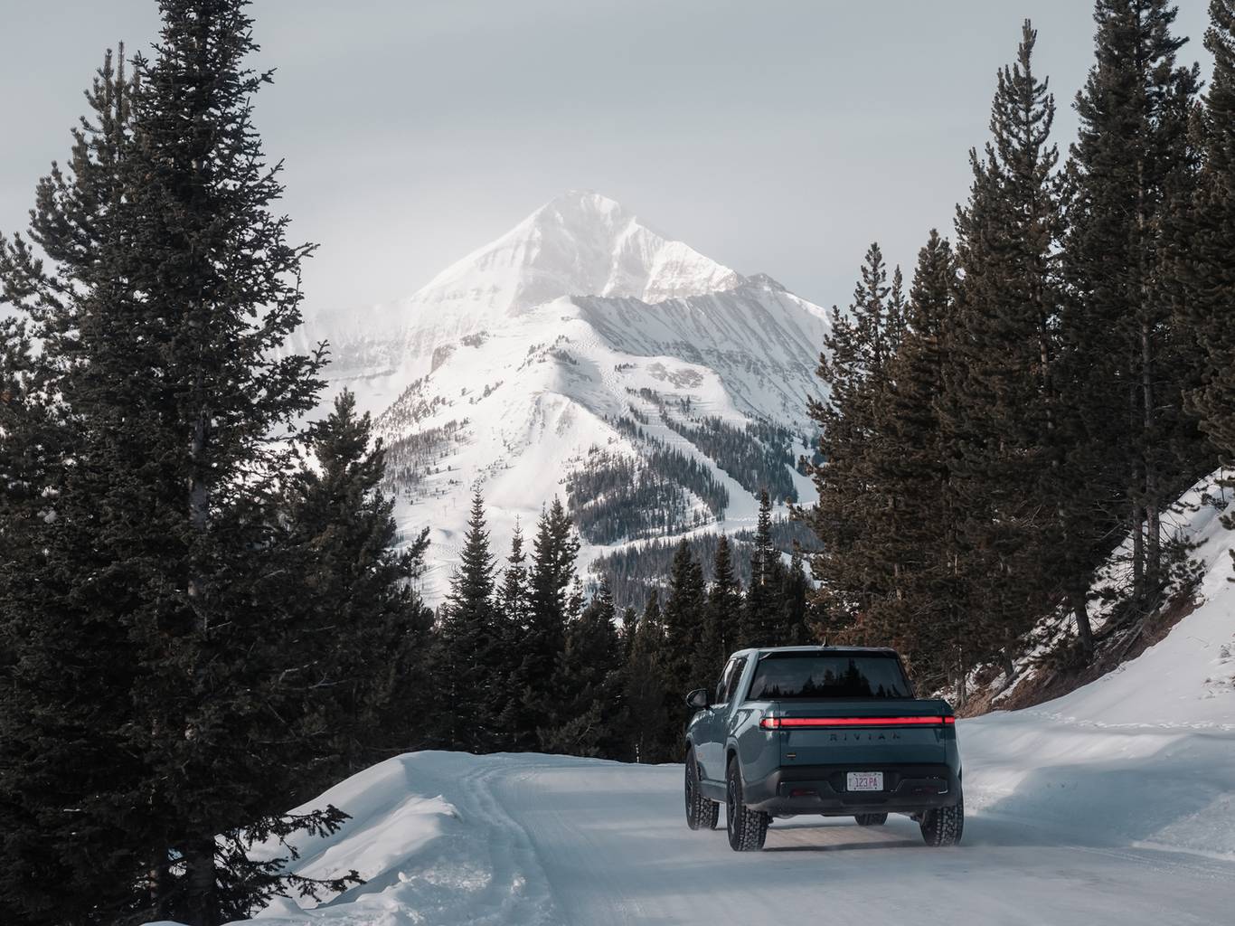 Rivian truck on a snowy road with Big Sky Resort in the background