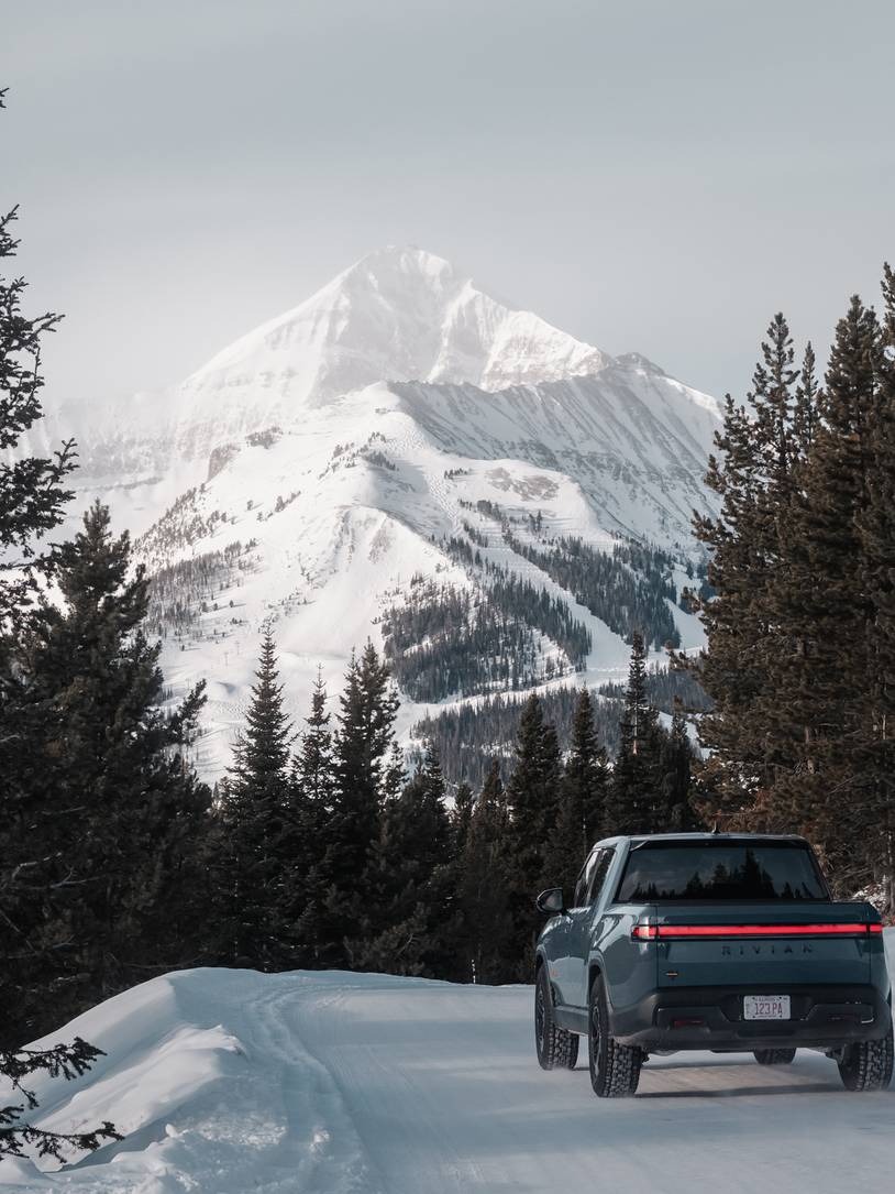 Rivian truck on a snowy road with Big Sky Resort in the background