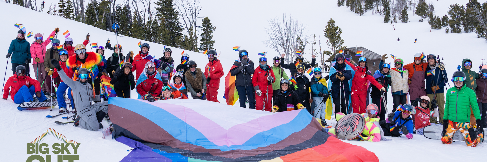 Group of skiers and snowboarders with a giant pride flag underneath Lone Peak