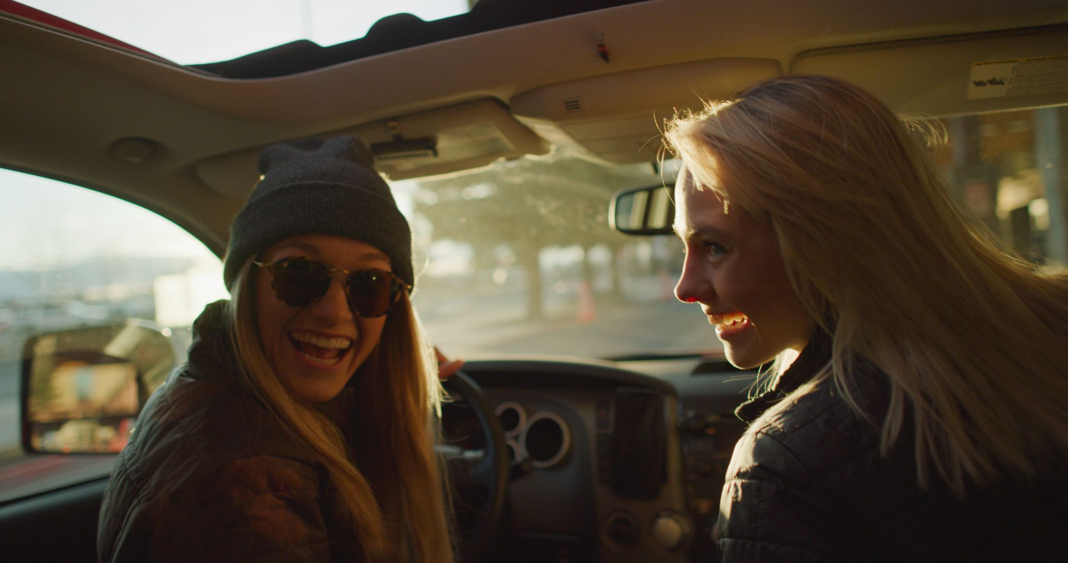 Two women in a car smiling at a person in the back seat