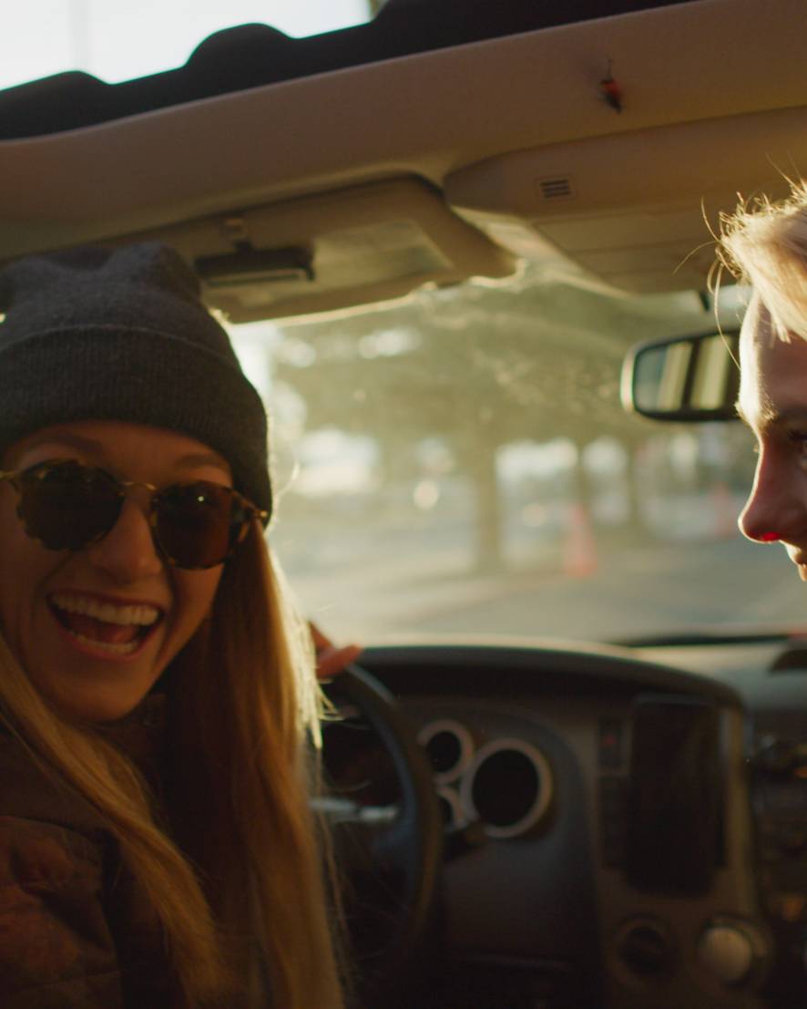 Two women in a car smiling at a person in the back seat