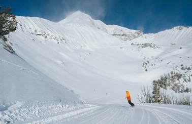 Snowboarder on a groomed run with Lone Peak in the background