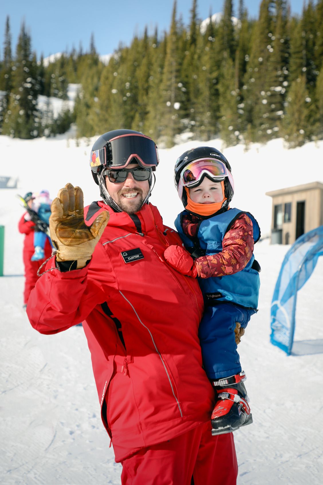 Child and instructor in ski gear waving to the camera
