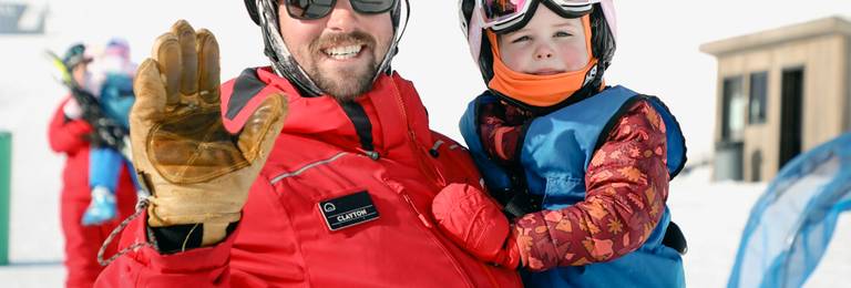 Child and instructor in ski gear waving to the camera
