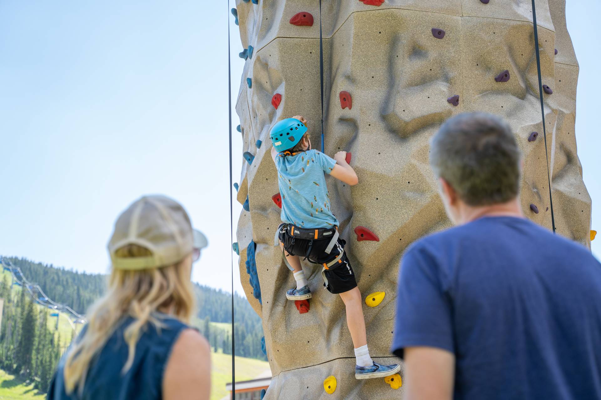Parents watching a boy climb a rock wall