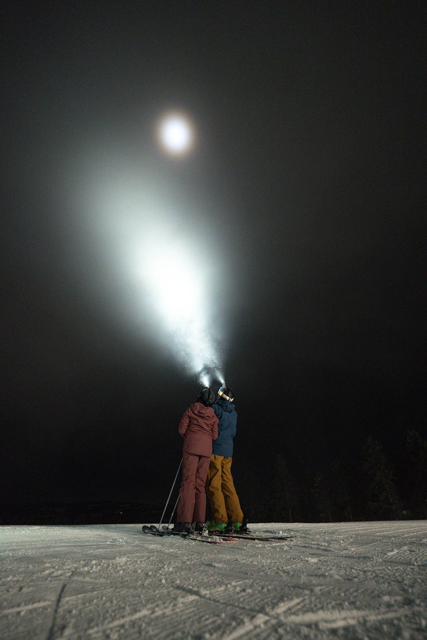 Two people in ski gear looking up at the night sky