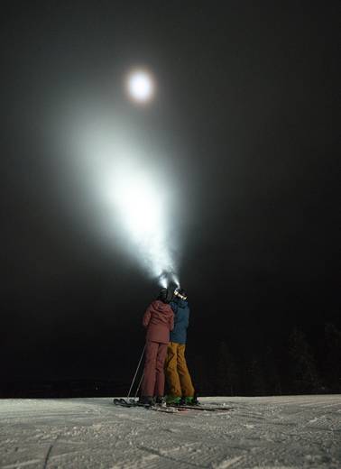 Two people in ski gear looking up at the night sky