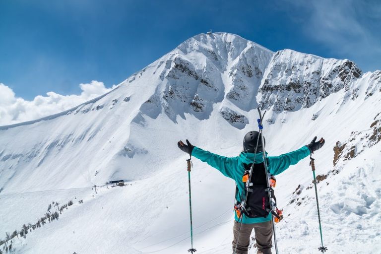 a skier lifts her arms and takes in the view from the ridge