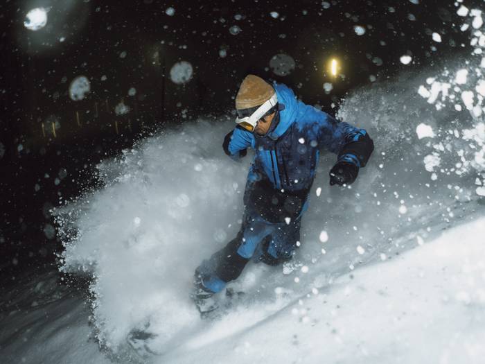Snowboarder riding powder at night at Brighton Ski Resort