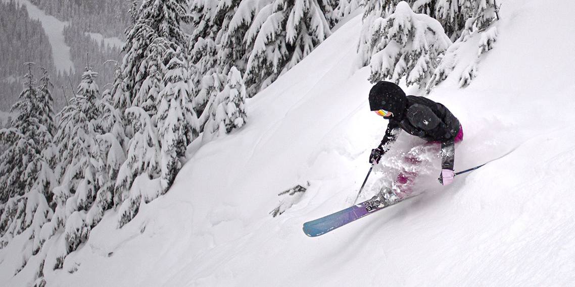 Skier in black jacket skis powder on Cypress Mountain through the trees.