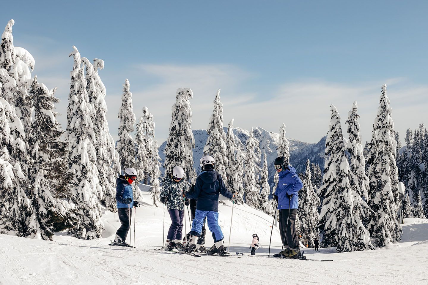 A ski instructor teaches three children on a slope surrounded by trees.