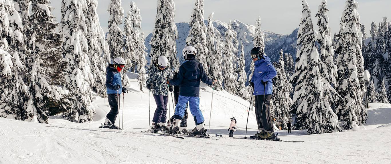 A ski instructor teaches three children on a slope surrounded by trees.