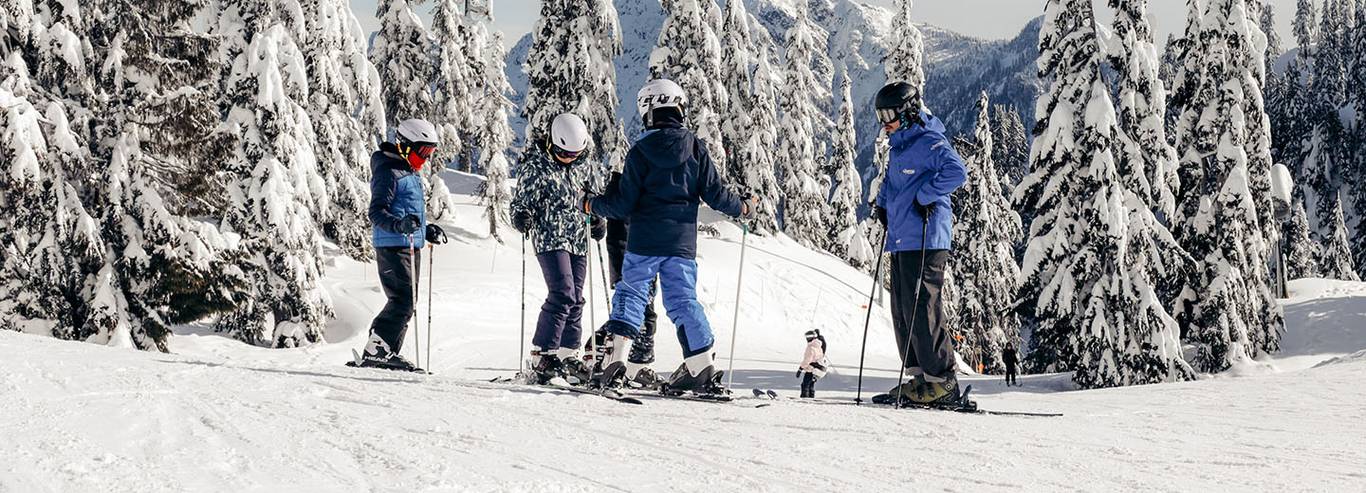 A ski instructor teaches three children on a slope surrounded by trees.