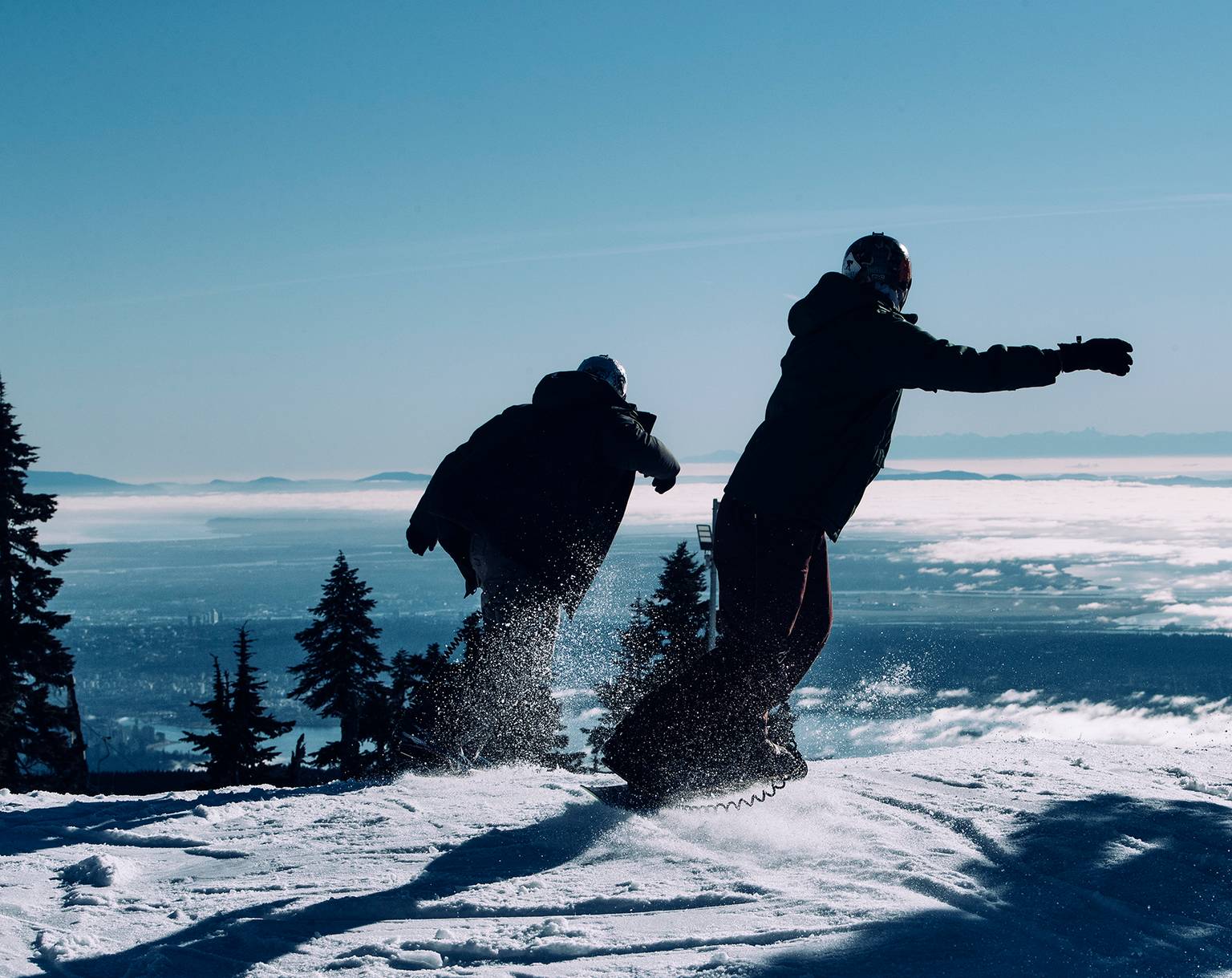 Two snowboarders with a view of the city in the background.