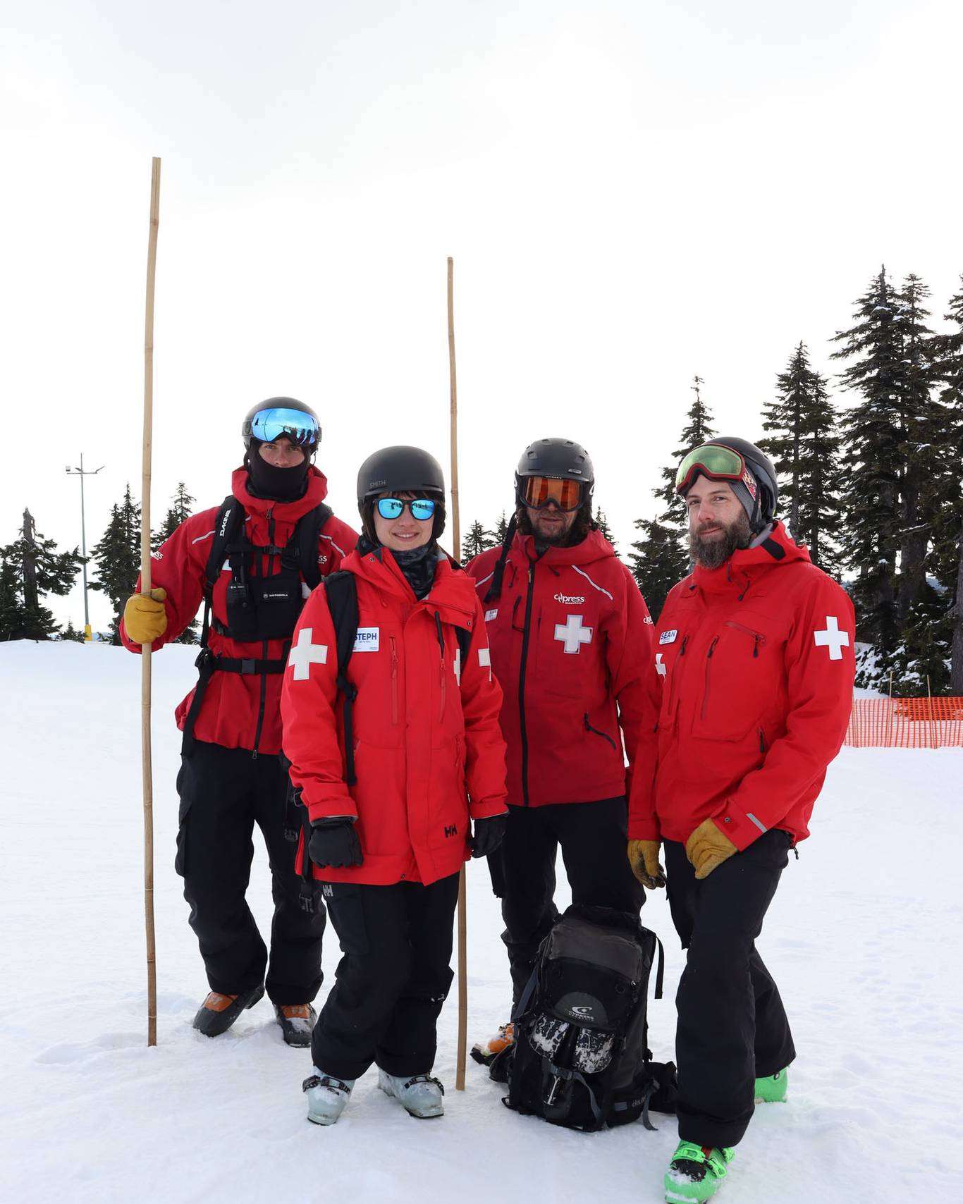 Four patrol staff posing with two of them holding bamboo sticks used for ski boundary.