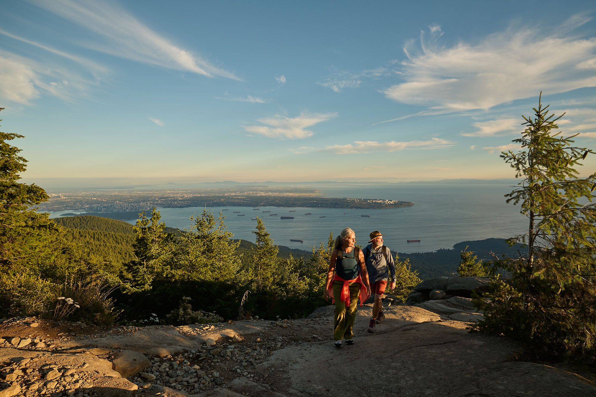 A couple hiking with views of the city and the ocean in the background.