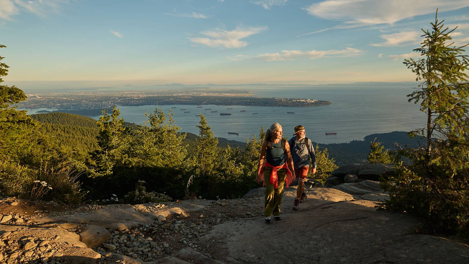 A couple hiking with views of the city and the ocean in the background.