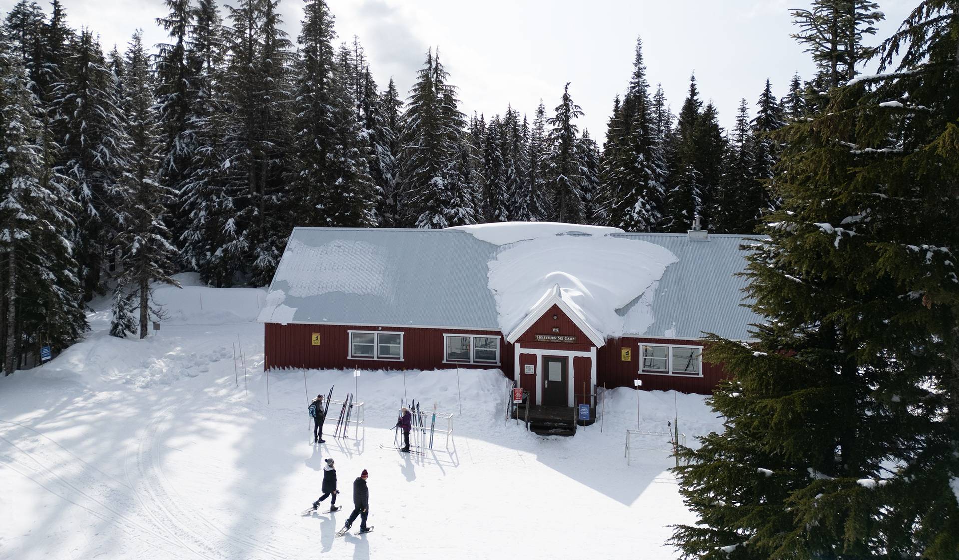 A red lodge in the winter time with guests milling around outside it.