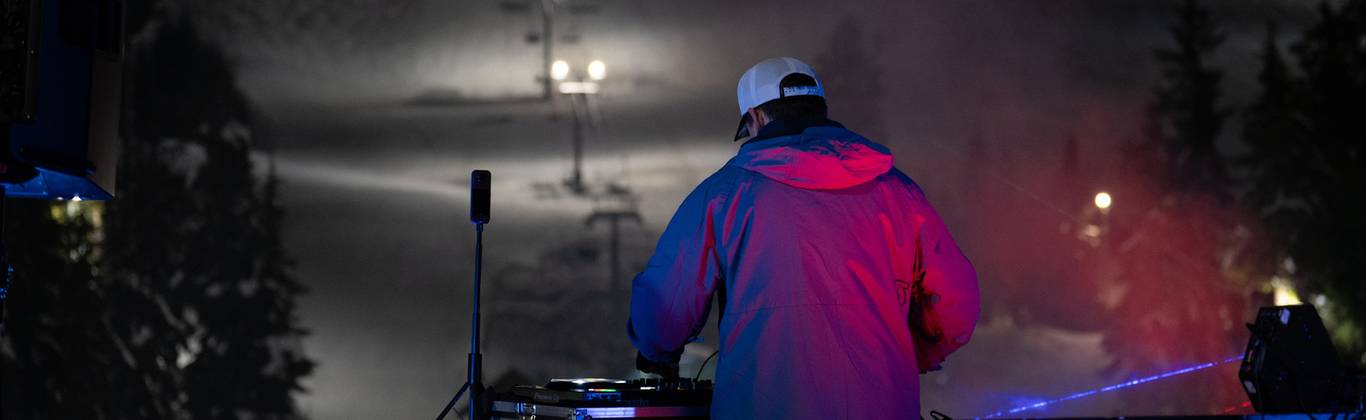 DJ plays music to crowd of people on a Cypress Mountain mountain top patio.