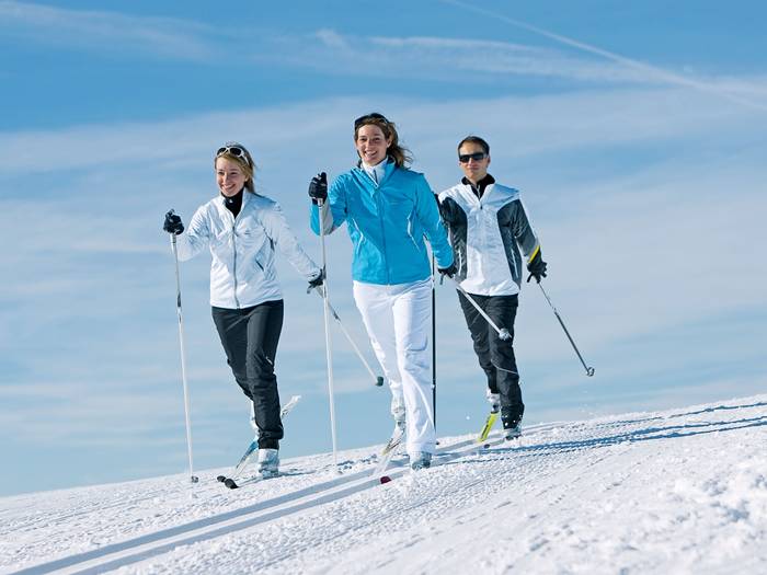 Three people cross country skiing on a sunny day.
