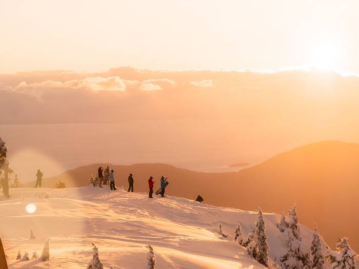 A group of people standing in the snow during a golden sunset.