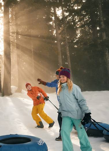 A family dragging snow tubes on snow during sunset.