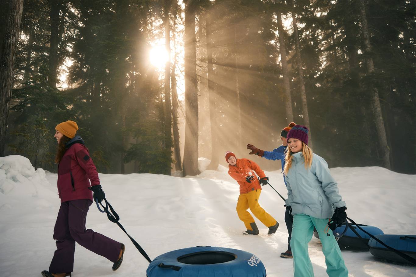 A family dragging snow tubes on snow during sunset.