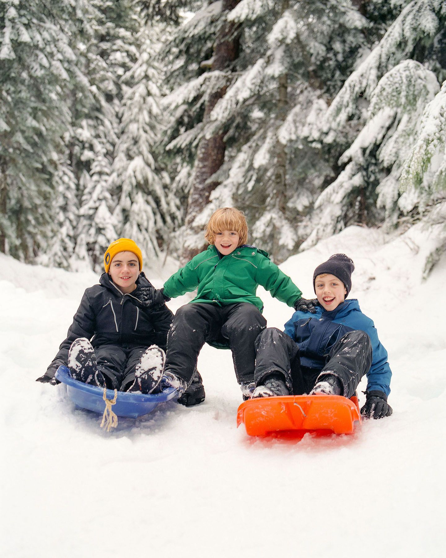 Three kids get ready to go sliding using colourful toboggans.