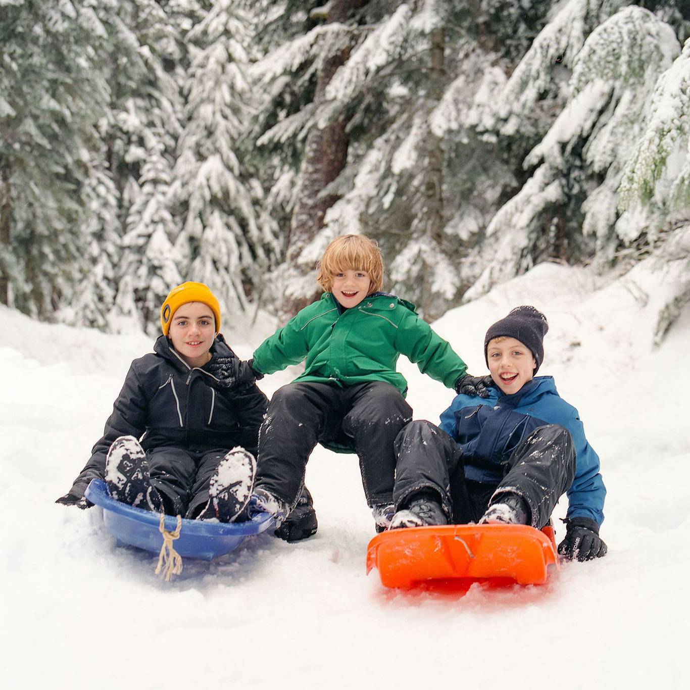 Three kids get ready to go sliding using colourful toboggans.