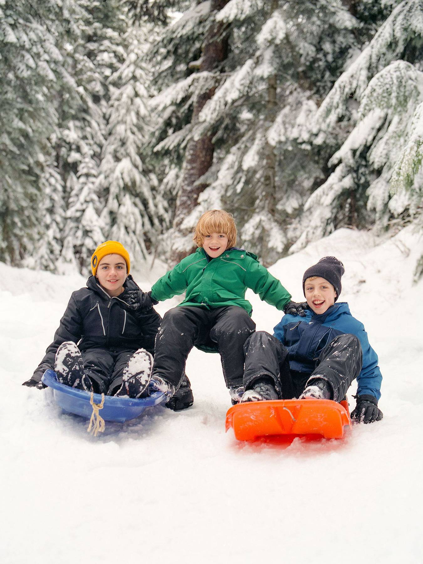Three kids get ready to go sliding using colourful toboggans.