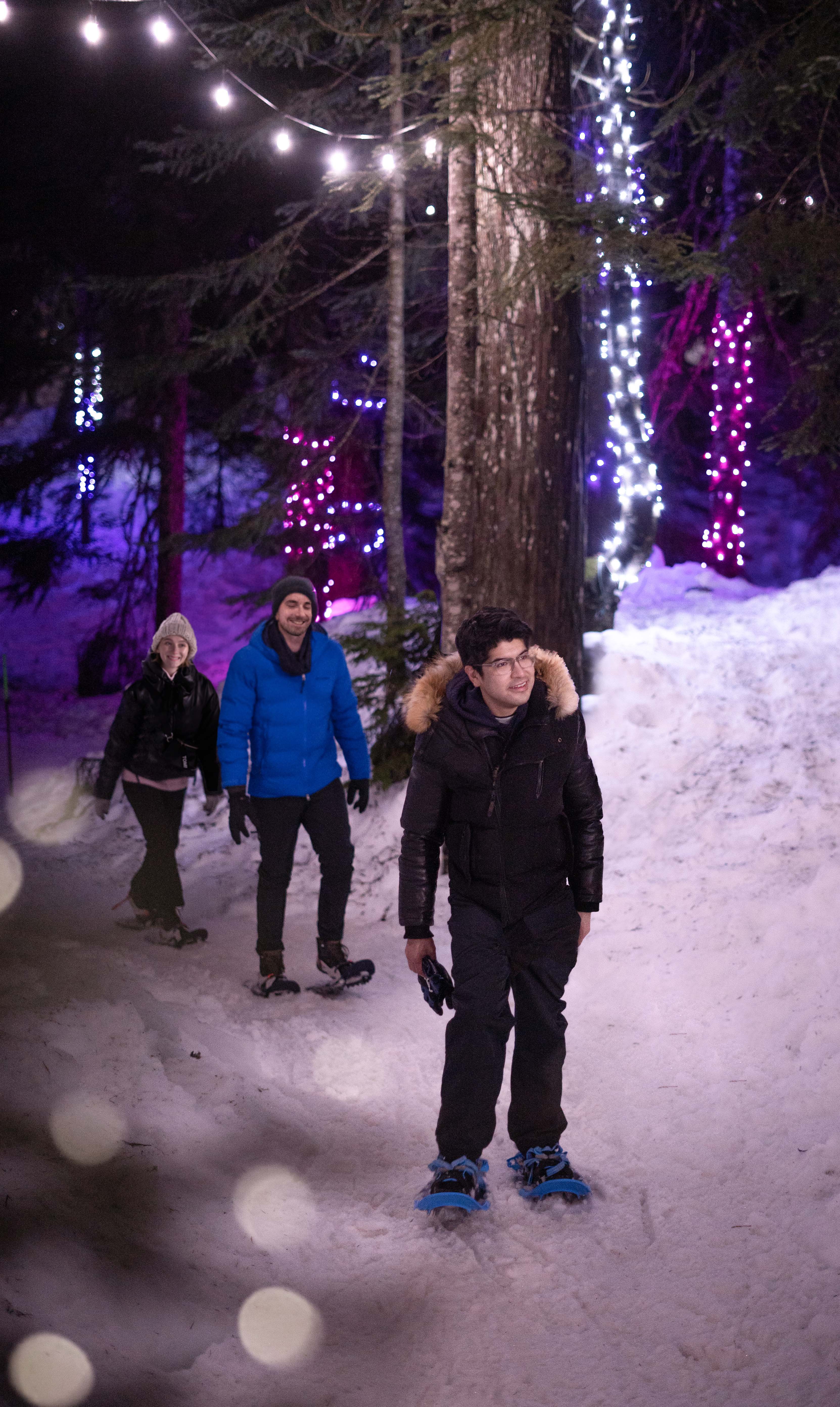 Friends snowshoeing at night with lights on trees.