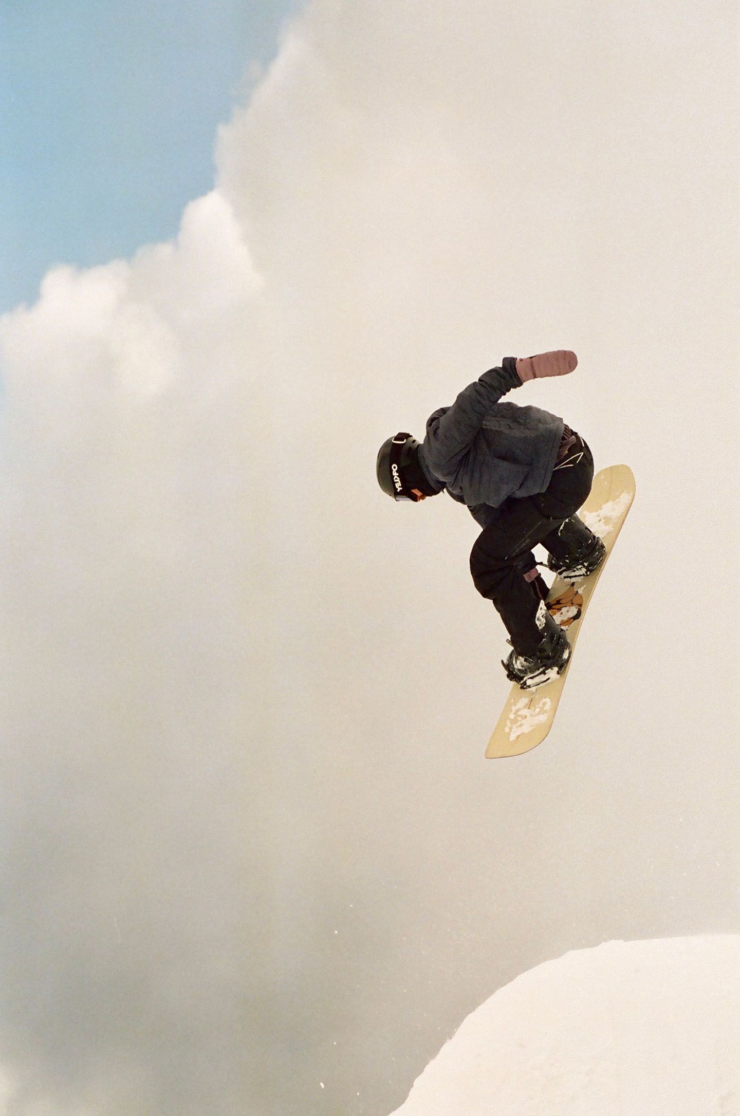A snowboarder grabs their yellow snowboard mid-air. 