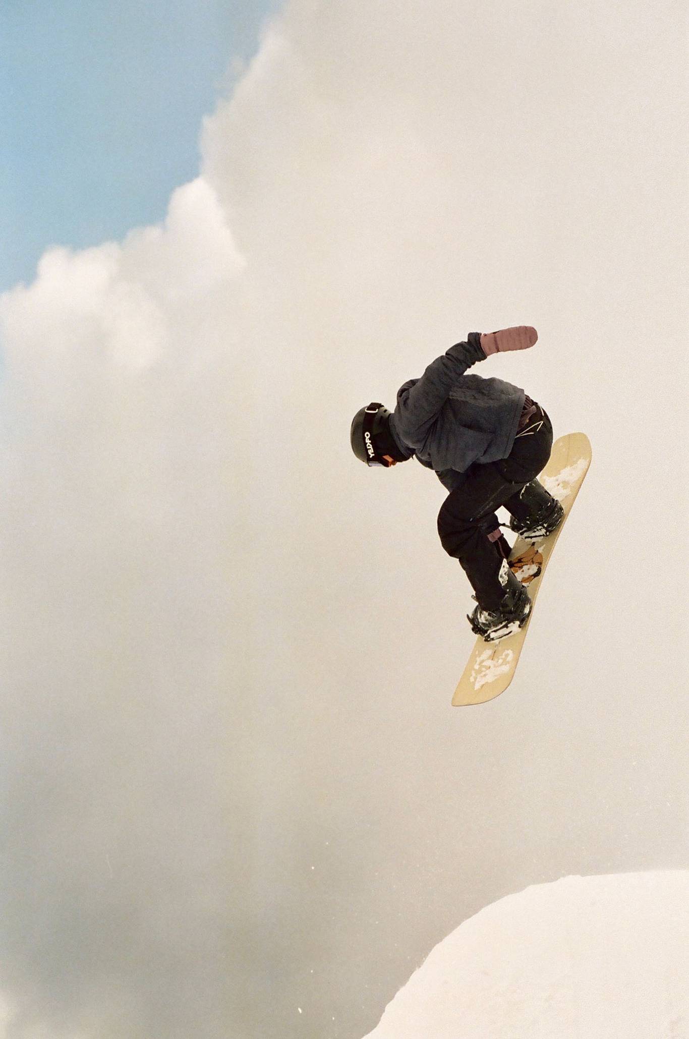 A person jumping with a yellow snowboard with fluffy clouds in the background.
